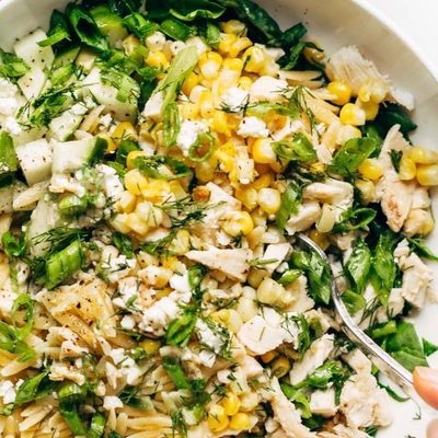 Hand holding Orzo Summer Salad in a bowl with fork.