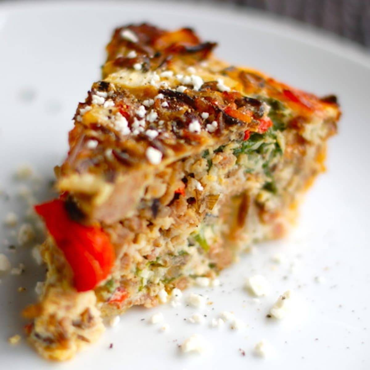 Sausage and red pepper quiche on a white plate.