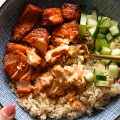 Air fryer salmon in a bowl with rice, cucumber, and sauce.