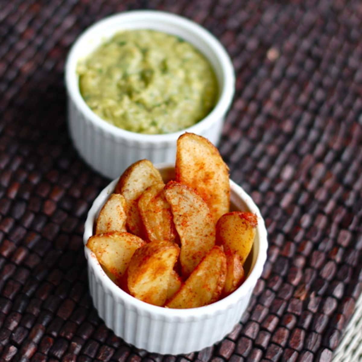 Avocado tomatillo dip in a white dish with potato wedges.