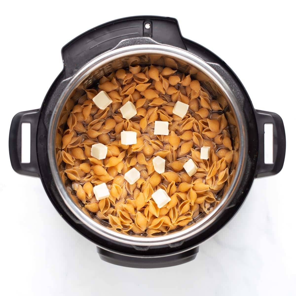 Uncooked mac and cheese in the Instant Pot with pieces of butter on top.