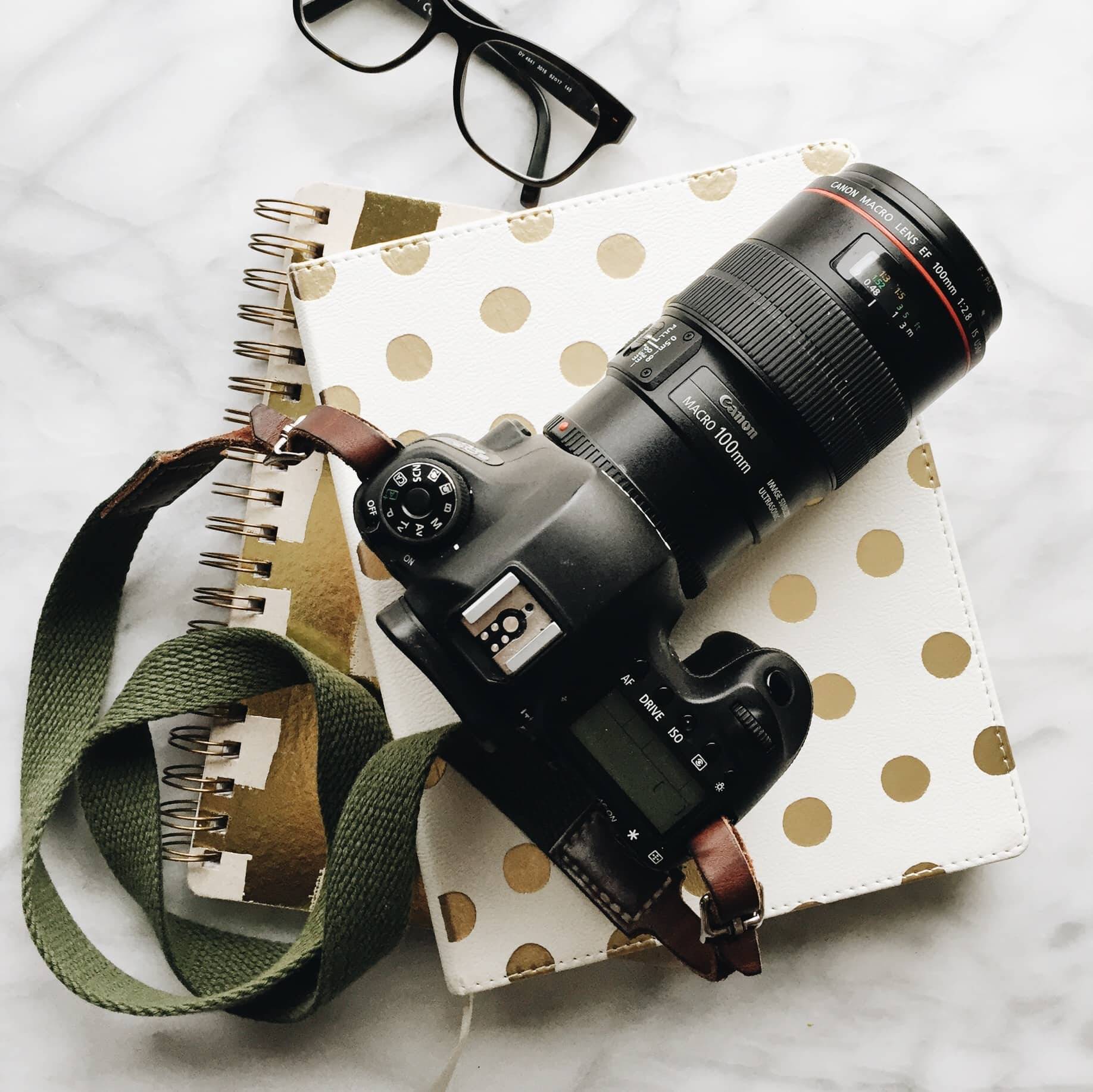 camera with green strap on two notebooks with glasses
